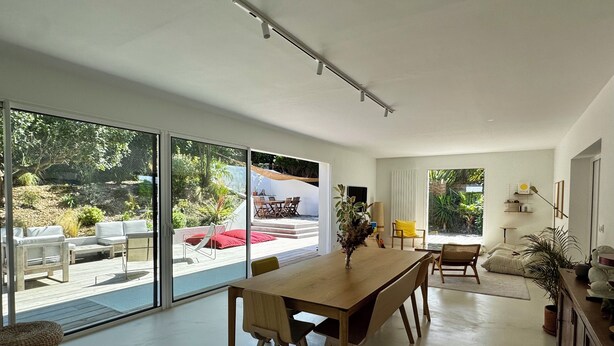 Un intérieur moderne avec une table à manger en bois, des chaises et une vue sur l’extérieur.