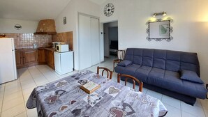 Un ambiente compatto con tavolo da pranzo, divano, angolo cottura e una sveglia appesa al muro.