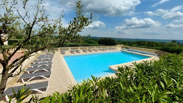Una piscina con lettini, circondata dal verde e con vista su dolci colline.