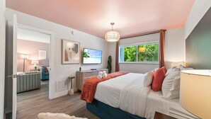 Quarto com cama, televisão, escrivaninha, cadeira, janela com vista e porta que dá para outro cômodo.