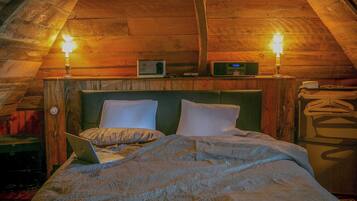 Une chambre mansardée chaleureuse, avec un plafond en pente en bois, un lit avec un ordinateur portable, deux lampes de chevet et une radio posée sur une étagère.