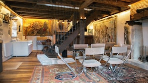 A spacious room with a wooden ceiling, a staircase, a dining area with chairs, and a patterned rug. - Twin houses on the Plateau de Millevaches (Croze)