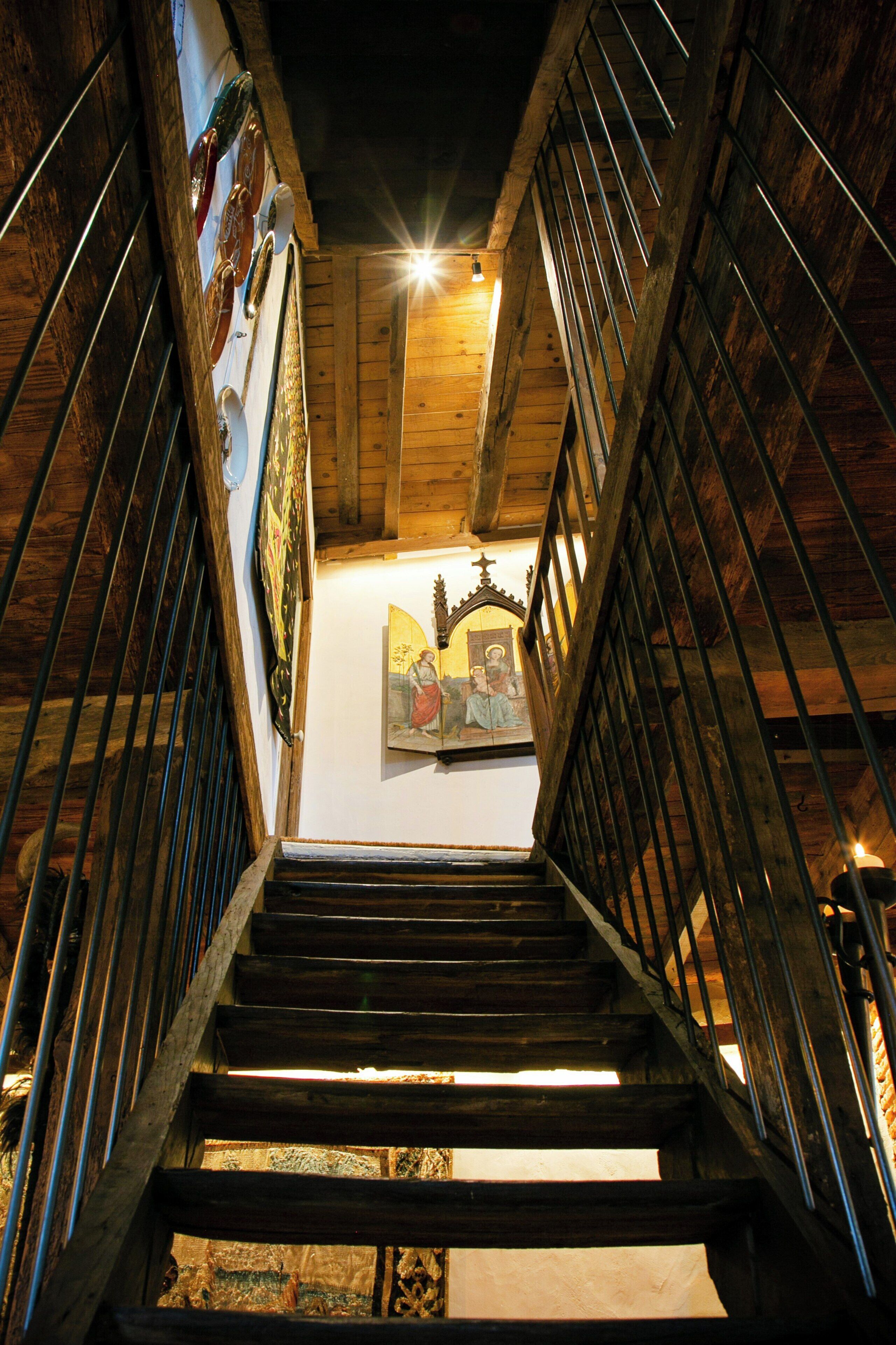 A wooden staircase with metal railings leading to a room with a framed artwork on the wall.