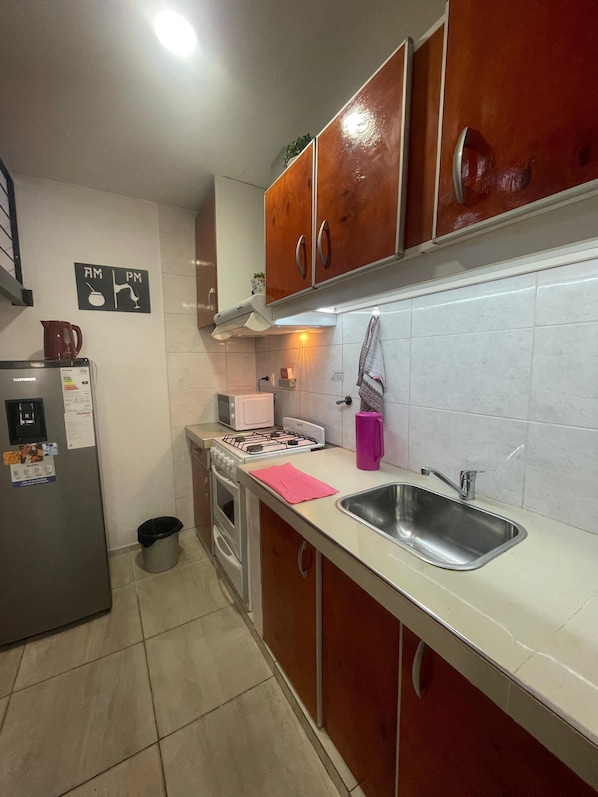 Una cocina con armarios de madera, un lavamanos de acero inoxidable, una estufa a gas y un refrigerador.