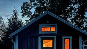 Eine kleine Holzhütte mit Satteldach, einer Haustür und zwei Fenstern mit orangenem Licht.