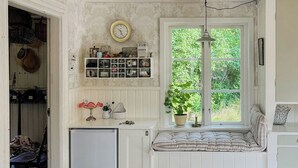 Eine Küche mit integriertem Kühlschrank, einem Fenster mit Blick auf Grünflächen, einer Uhr und einem Regal mit Küchenutensilien.