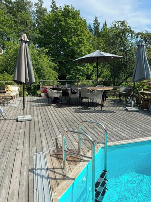 A wooden deck with a pool, outdoor furniture, and umbrellas. - Charming 1900s Cottage in Billinge Village (Norrtälje)