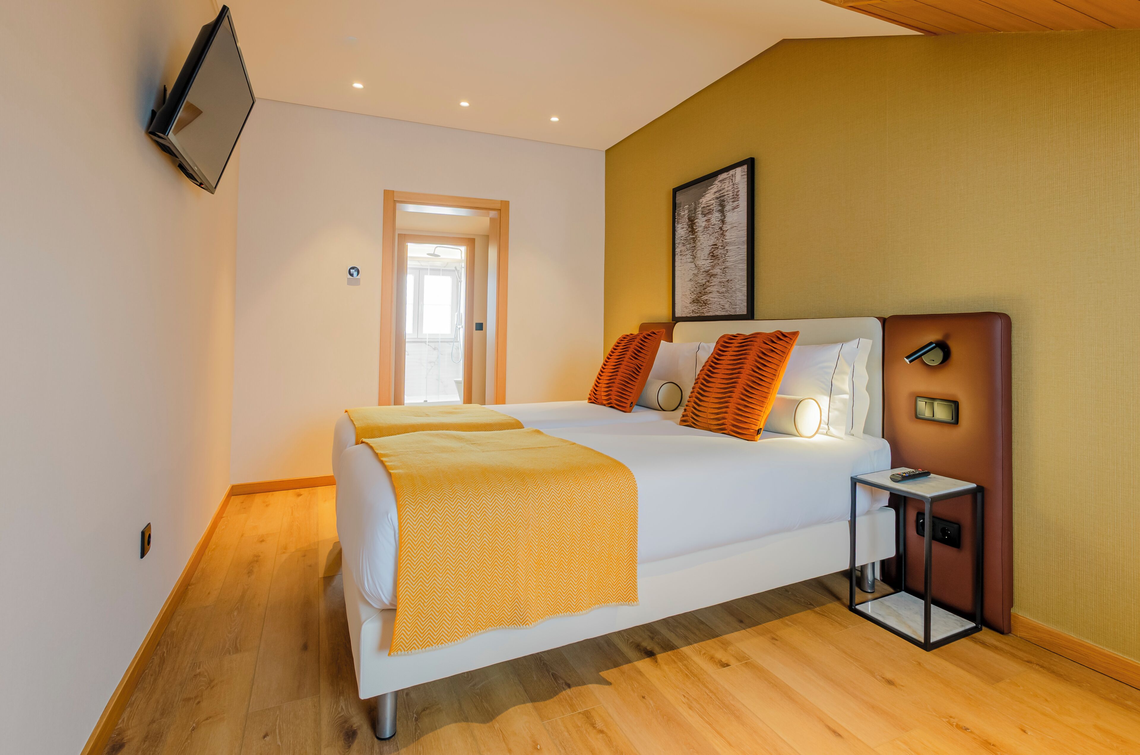 A modern hotel room with a bed, bedside table, and a television mounted on the wall.