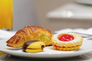 Un plato con un croissant, una banana cubierta de chocolate y un pastelito con relleno rojo.
