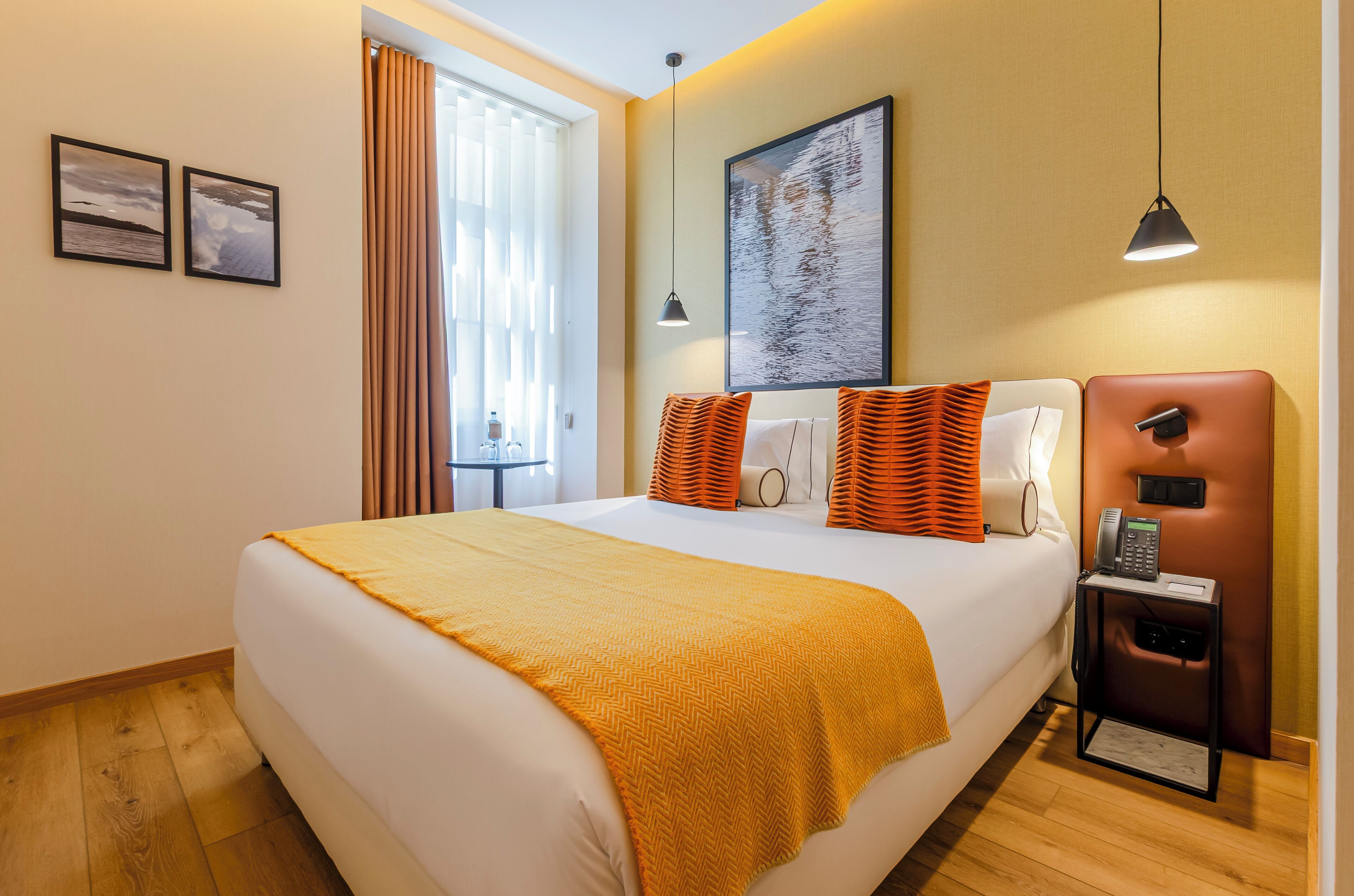 A hotel room with a bed, a desk with a telephone, and a window with curtains.