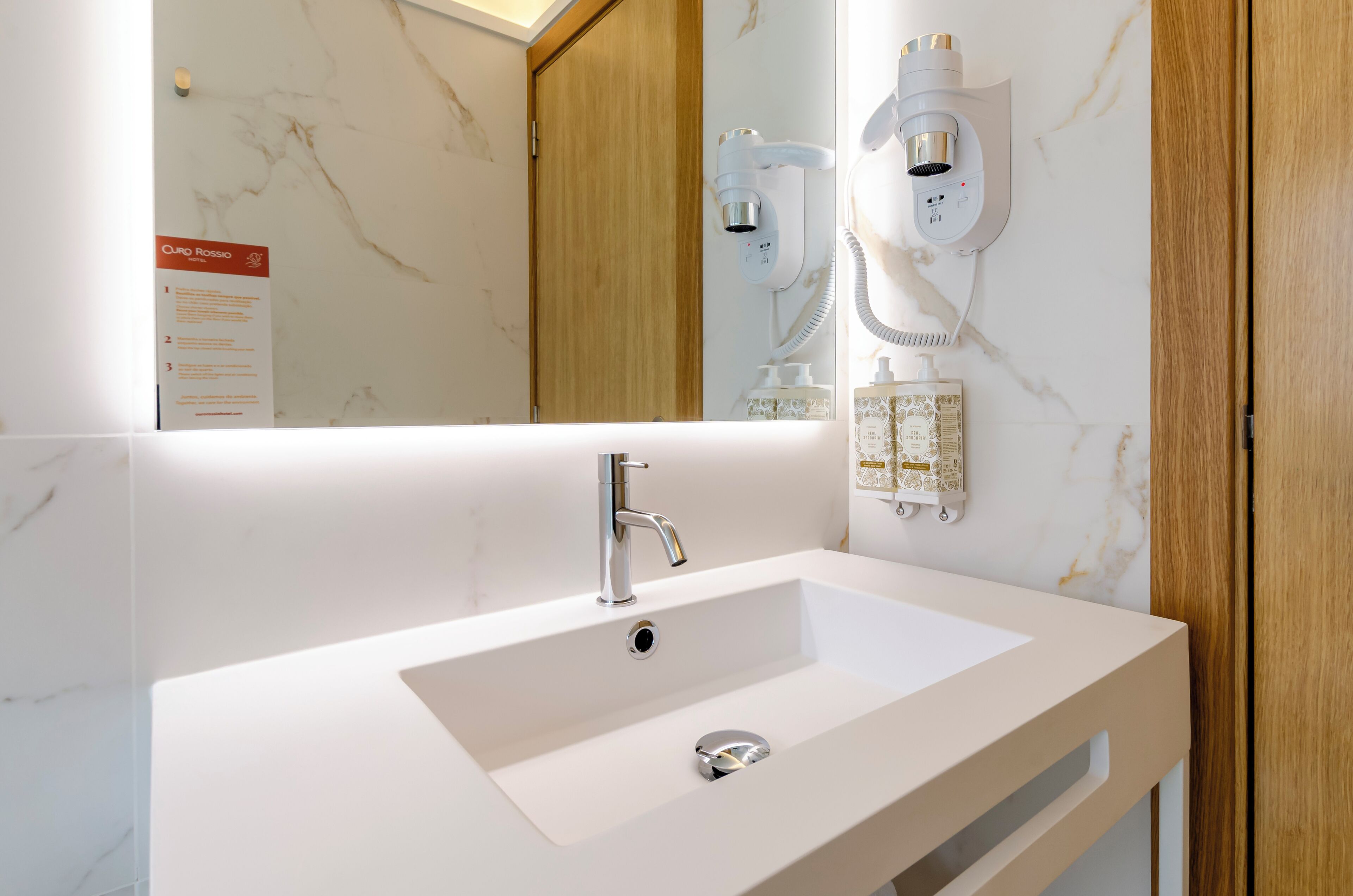 A modern bathroom with a white sink, a mirror, and a wall-mounted hairdryer.