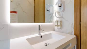 A modern bathroom with a white sink, a mirror, and a wall-mounted hairdryer.