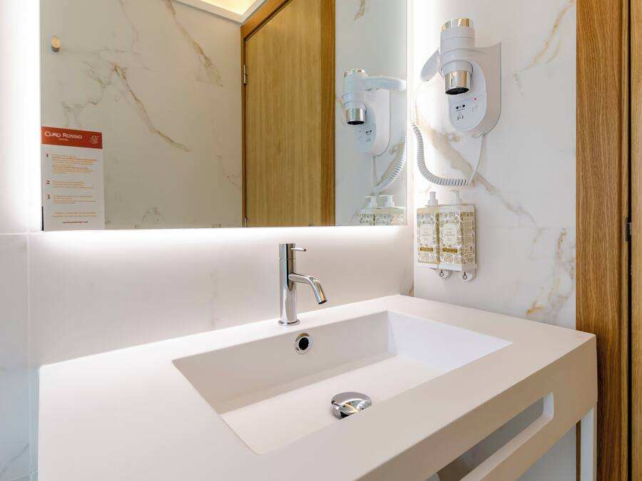 A modern bathroom with a white sink, a mirror, and a wall-mounted hairdryer.