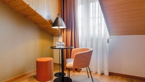 Una habitación pequeña con una mesa redonda, una silla, una lámpara y un reposapiés rojo.
