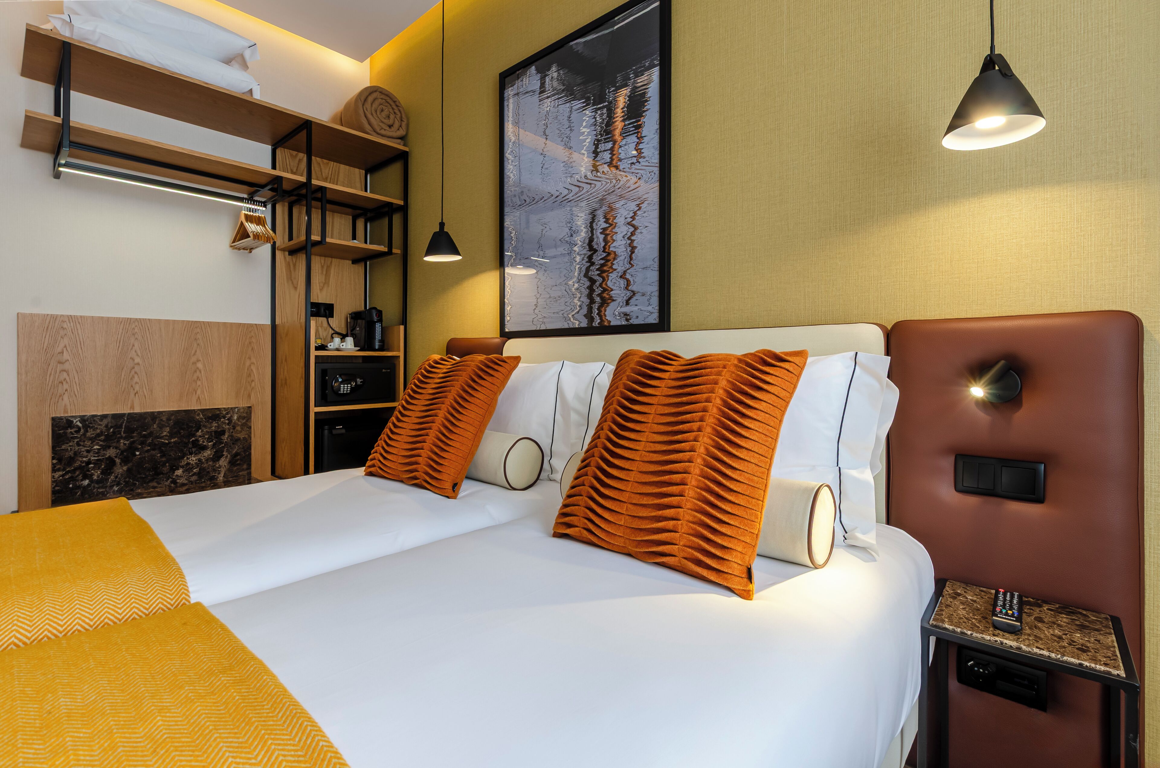 A hotel room with a bed, a coffee machine, a TV, and a painting on the wall.