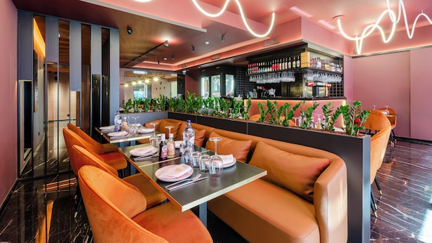 Un restaurante con zona de bar, asientos con cojines naranja y un diseño de luces de neón en el techo.