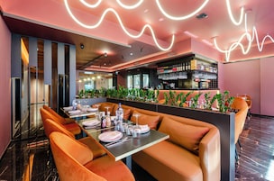 A restaurant with a bar area, seating with orange cushions, and a neon light design on the ceiling.