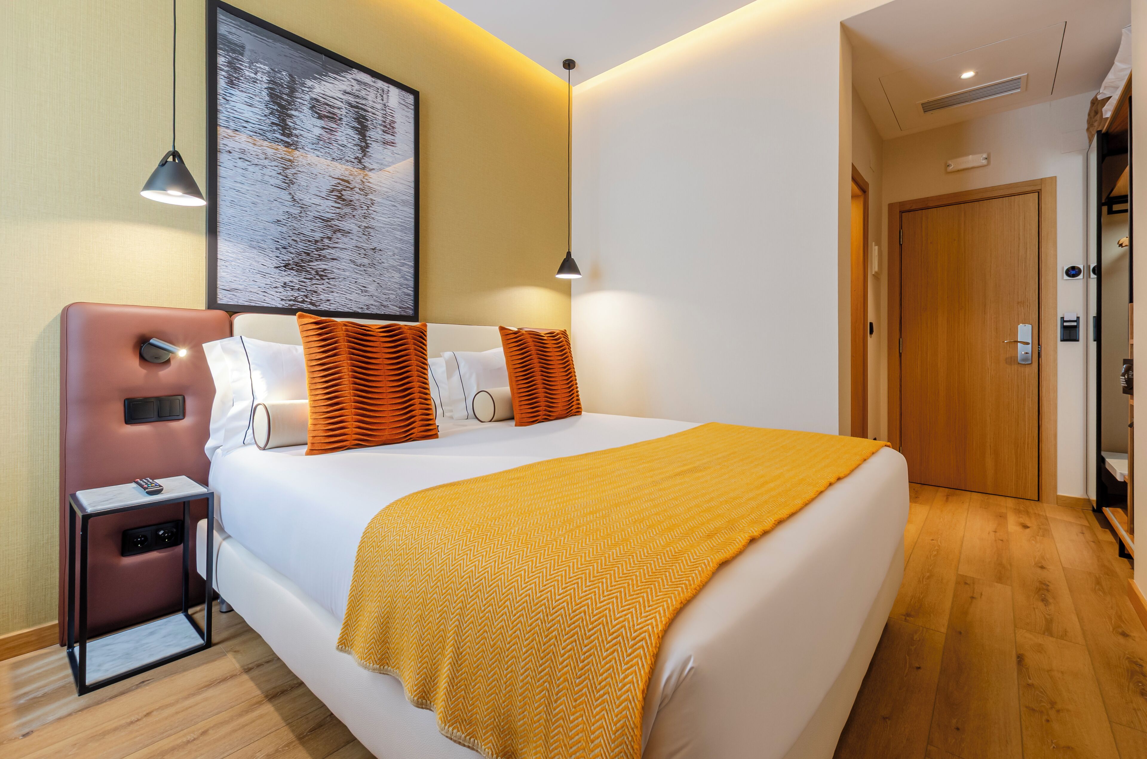 Une chambre d’hôtel avec un grand lit, une table de chevet, une commode, une œuvre d’art accrochée au mur et une porte.