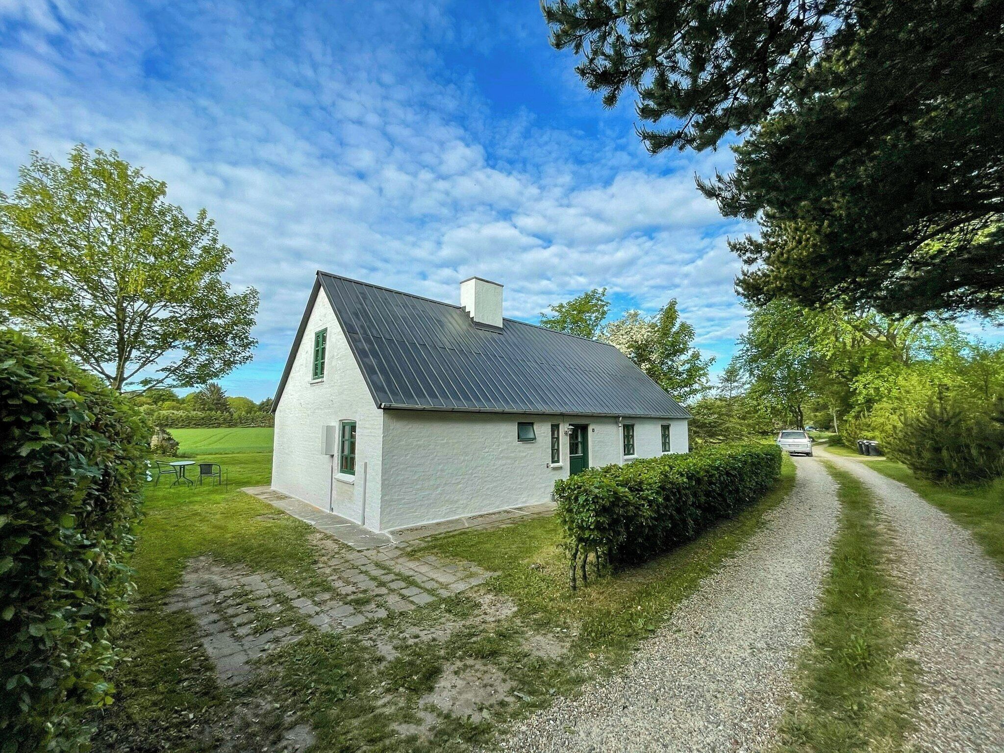 A white house with a grey roof, a gravel driveway, and a car parked on the side.