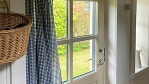 Une porte blanche avec une fenêtre, un rideau à carreaux et un panier en osier accroché au mur.