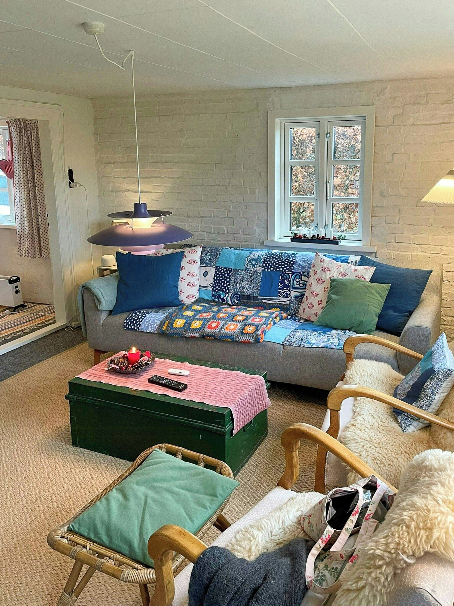 Ein gemütliches Wohnzimmer mit einer Couch, einem grünen Hocker, Korbstühlen und einem Fenster mit Blick.