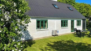 Une maison de plain-pied avec un toit sombre, des murs extérieurs blancs, des encadrements de fenêtres verts et un petit garage attenant.