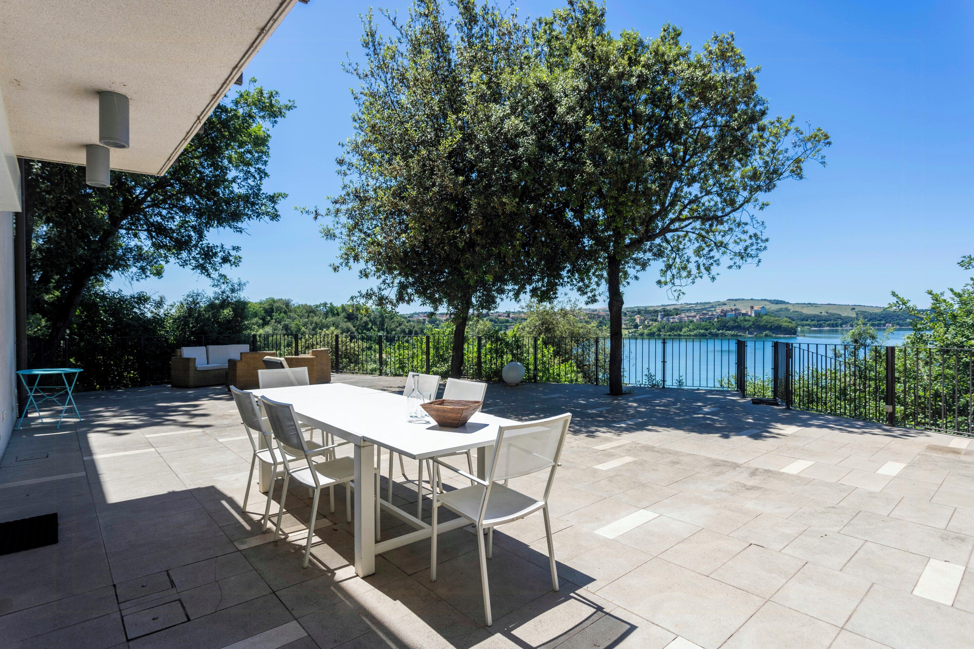 Un patio al aire libre con una mesa y sillas, vistas a un lago y un árbol.