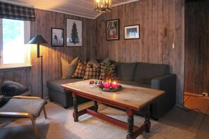 A cozy living room with a wooden wall, a sofa, a coffee table with candles, and framed pictures. - Charming cabin in Vikerfjell (Hønefoss)