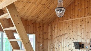 Puinen sisustus, jossa on portaikko, kulmasohva, sohvapöytä ja kattokruunu.