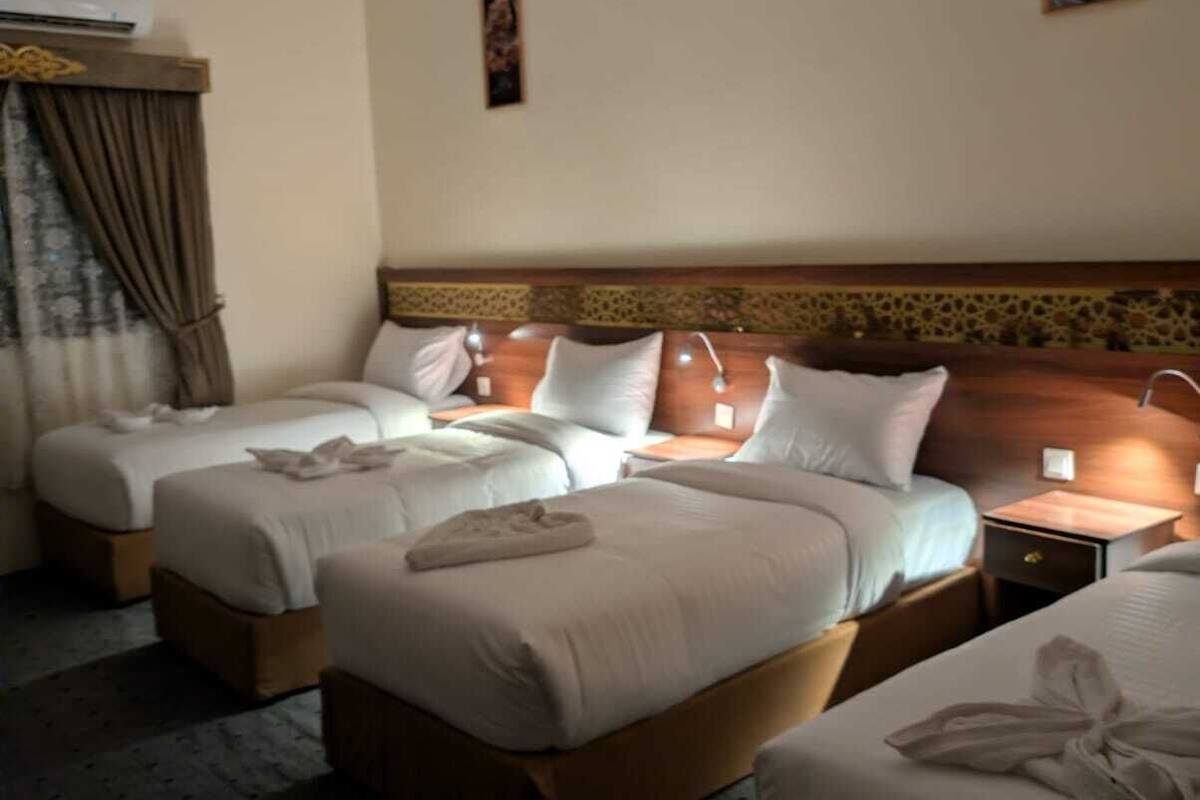 Hotellihuone, jossa on kaksi sänkyä, yöpöytä, lamppu ja taulu seinällä.