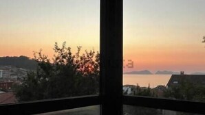 Ein Fenster mit Blick auf einen Sonnenuntergang über Wasser, Gebäude und Bäume.