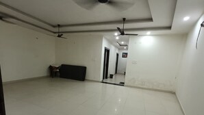 A spacious room with a tiled floor, ceiling fans, and a dark-colored sofa. - Hotel Shriji Nikunj (Mathura)