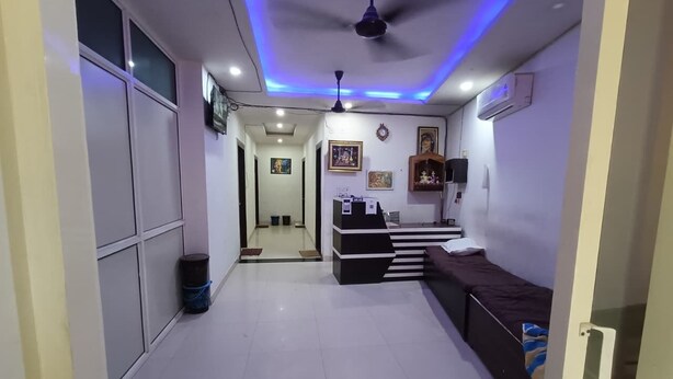 A hotel corridor with a reception desk, a bed, and a ceiling fan. - Hotel Shriji Nikunj (Mathura)