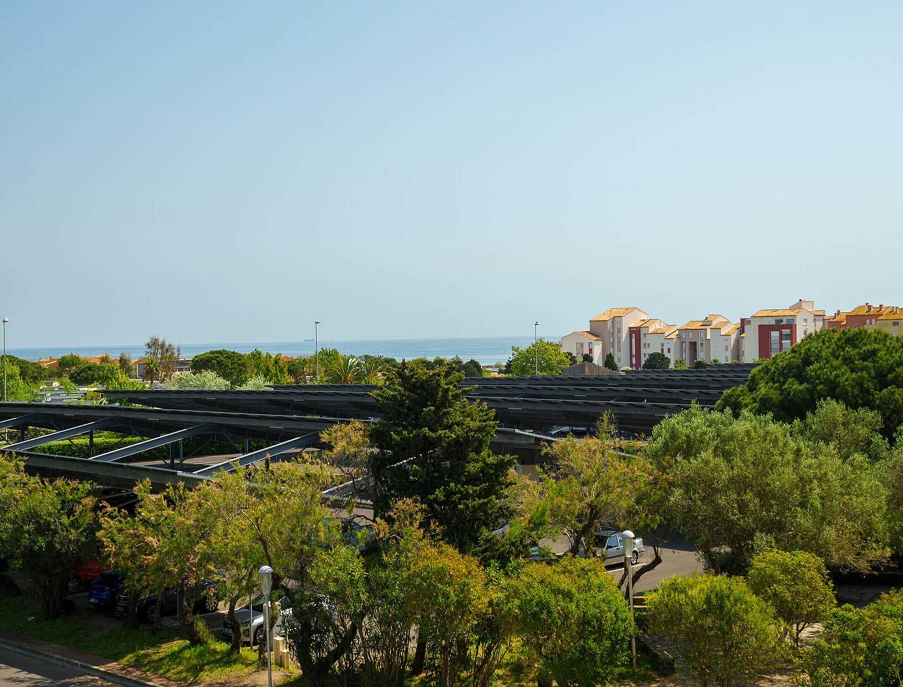 Zona residencial a la costa, amb aparcament, vegetació i edificis amb portes vermelles.