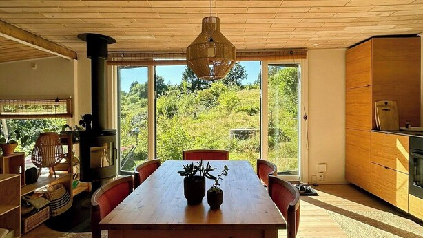 Ein Essbereich mit Holztisch und -stühlen, einer Pendelleuchte und großen Fenstern mit Blick auf Grünflächen.