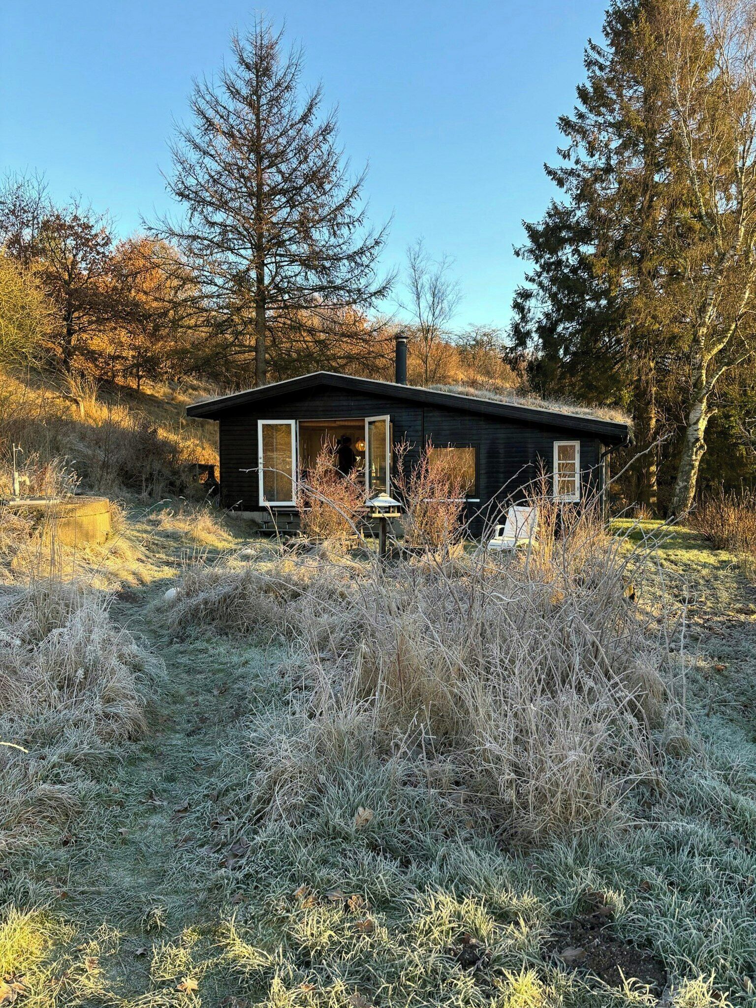 Une petite cabane avec un toit en pente, une cheminée et une porte dotée de panneaux de verre.