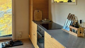 Eine moderne Küche mit Holzausstattung, einem eingebauten Ofen und einem Fenster mit Blick auf Bäume.