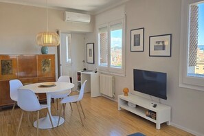 A modern living room with a dining area, a flat-screen TV, and artwork on the walls. - Opening Doors Montjuïc-Sants, bright and incredible views (Barcelona)
