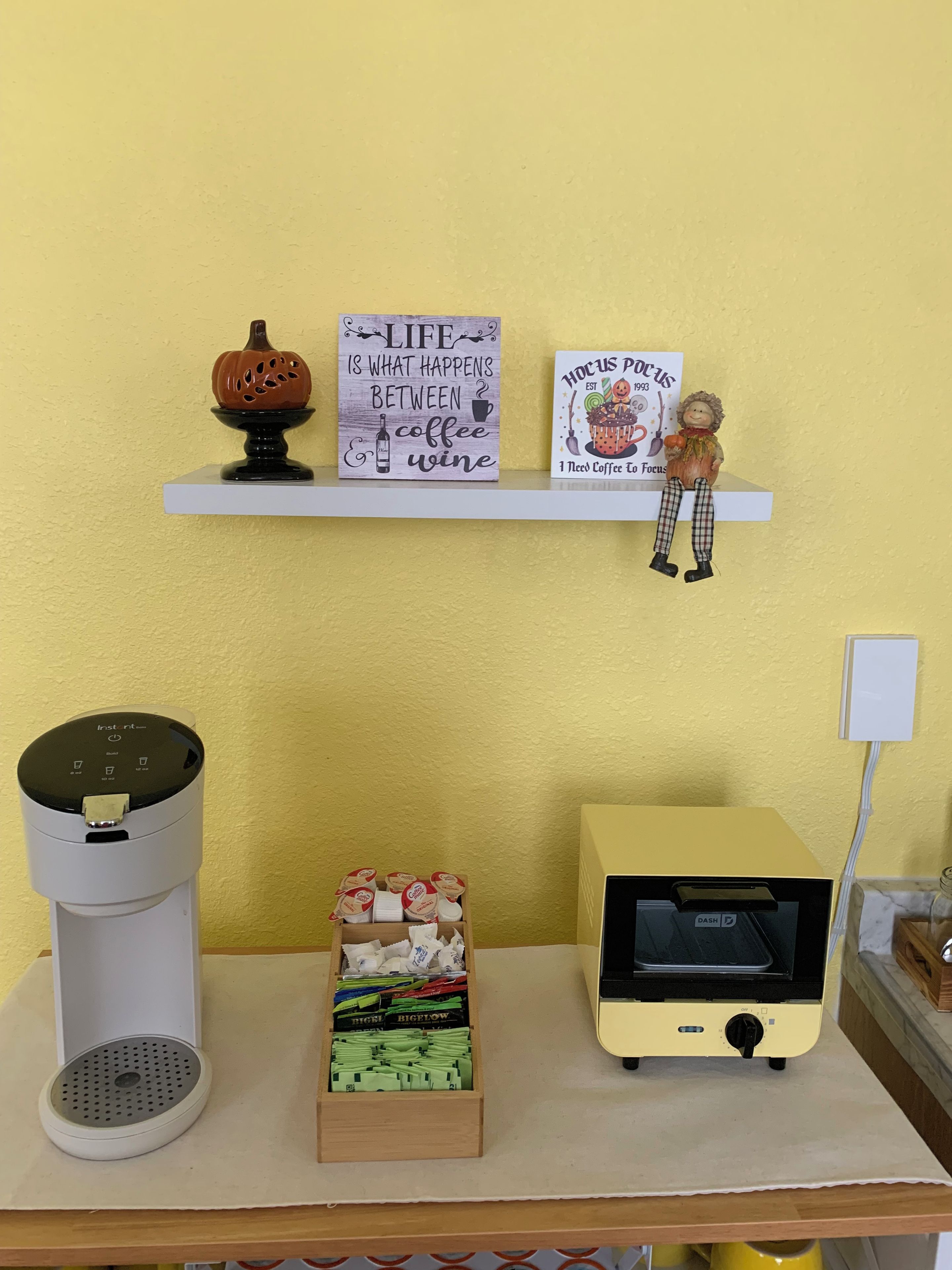 Eine Küchenzeile mit Kaffeemaschine, Mikrowelle, einer Kapselbox und einem Regal mit Dekoration.
