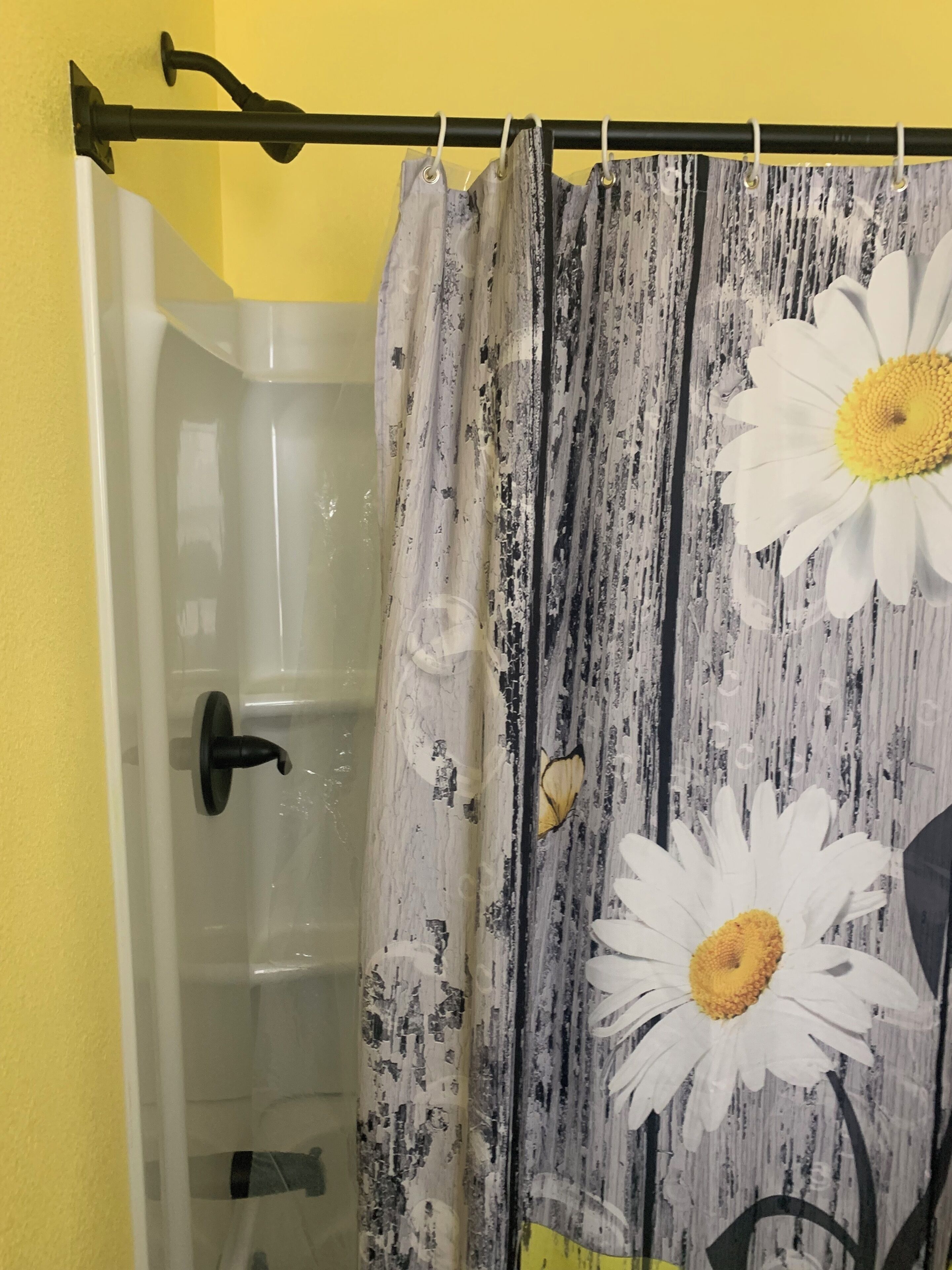 Un baño con cortina de ducha estampada con diseños de margaritas, una bañera y una pared amarilla.