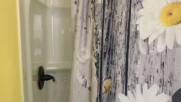 Un baño con cortina de ducha estampada con diseños de margaritas, una bañera y una pared amarilla.