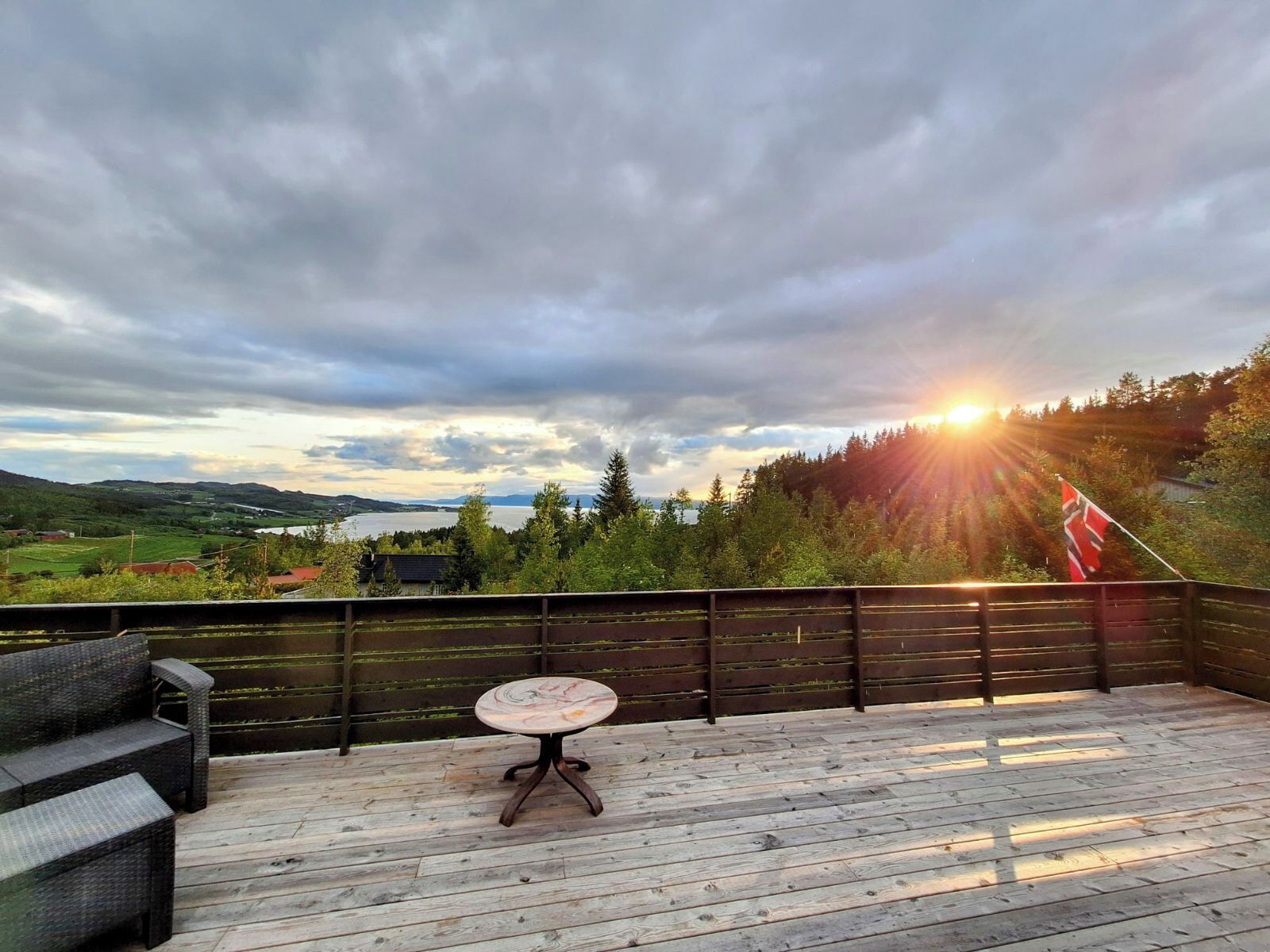 A wooden deck with a table and benches, overlooking a scenic landscape with a lake and mountains.