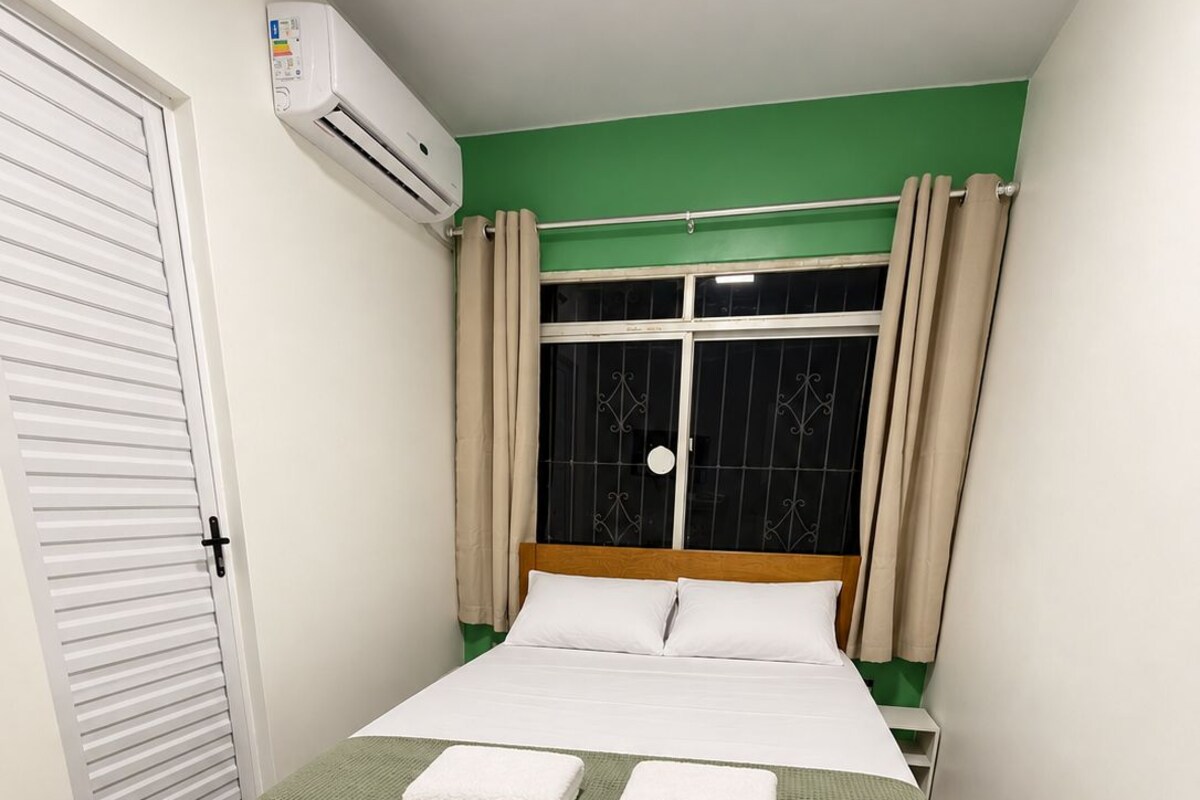 Ein Schlafzimmer mit einem Bett, einem Fenster mit Vorhängen, einer Klimaanlage und einer Tür.