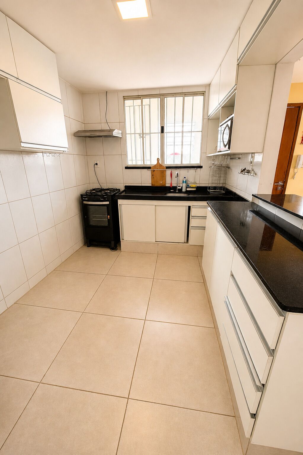 A kitchen with white cabinets, a black countertop, a stove, and a window with blinds.