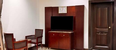 A room with a wooden cabinet, a flat-screen TV, two chairs, and a door.