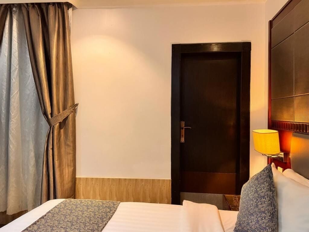 Une chambre d’hôtel avec un lit, une porte, une lampe et des rideaux.