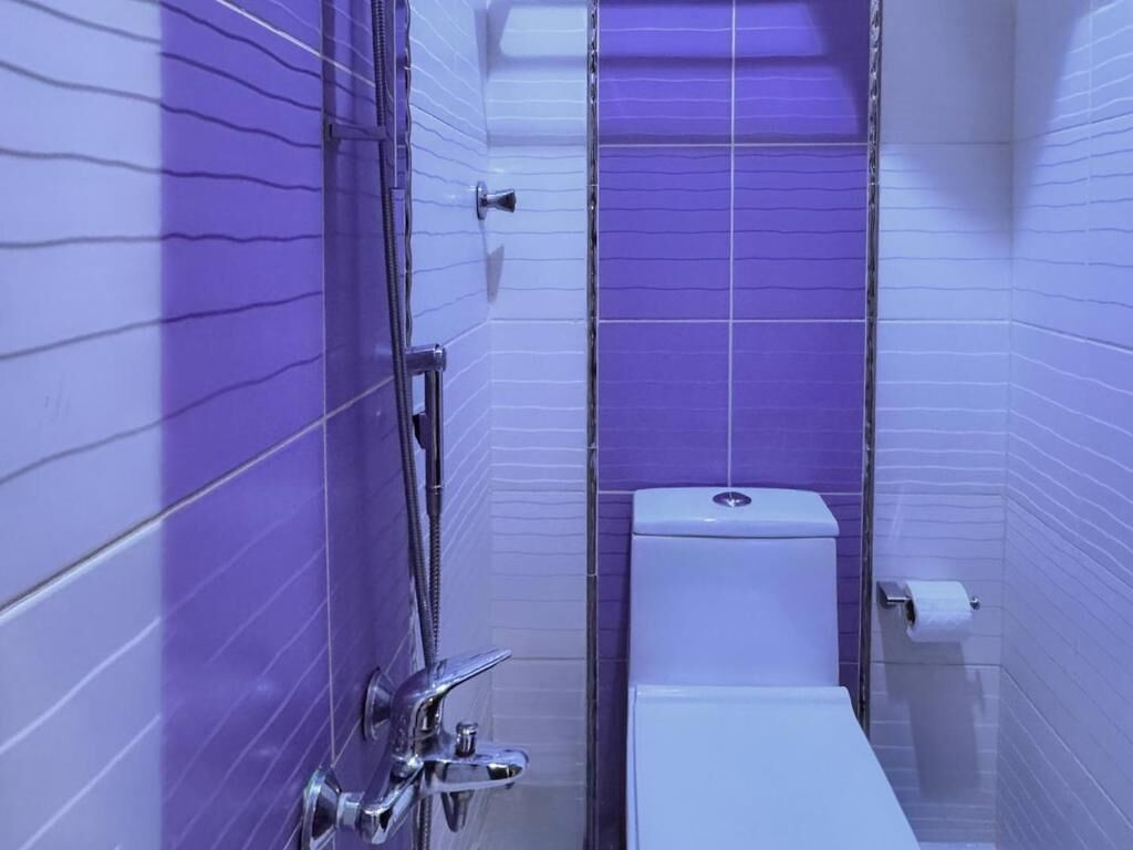 A bathroom with purple tiled walls, a white toilet, and a chrome shower fixture.