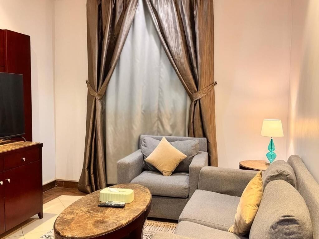 A living room with a sofa, armchair, and a small round table with a remote control.