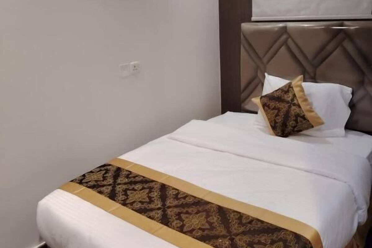 A neatly made bed with a patterned bedspread, a headboard with a diamond pattern, and a window with a blind.