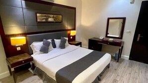 A hotel room with a bed, bedside lamps, a nightstand, a dresser, a mirror, and an air conditioning unit. - Quiet Rooms 12   (Riyadh)